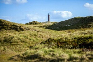 Ein Leuchtturm auf einer grasbewachsenen Anhöhe bei blauem Himmel.