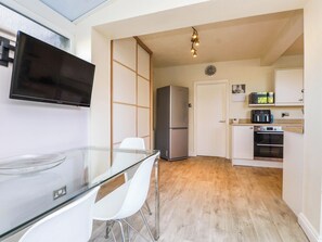 Eine kleine Küche mit Kühlschrank, Mikrowelle, Backofen und einem Glastisch mit Stühlen.
