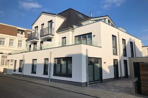 Un edificio residencial moderno de dos pisos con balcón, ventanas grandes y techo plano.