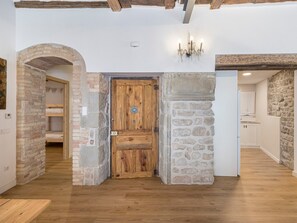 A room with a wooden door, stone walls, a chandelier, and a visible kitchen area. - Apartment 'Pèndol' with Balcony, Wi-Fi and Air Conditioning (Solsona)