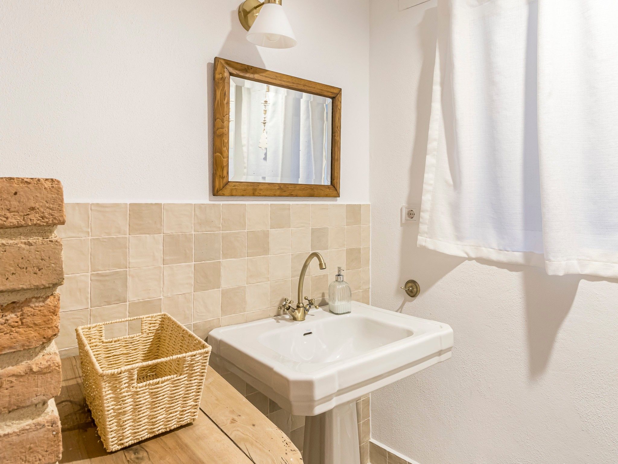 Un baño con un lavamanos blanco, un espejo, una toalla colgada en la puerta y una cesta de mimbre.