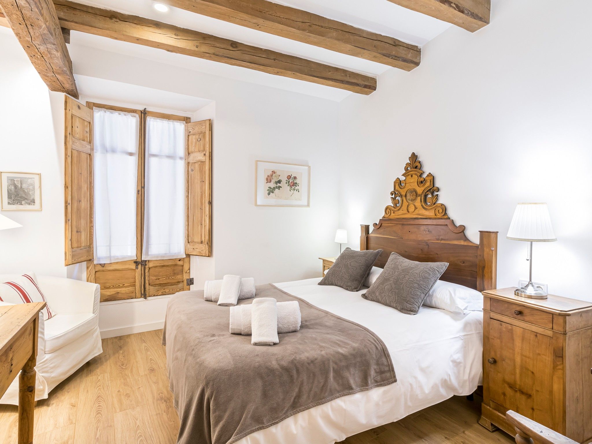 A bedroom with a wooden headboard, a bed with white linens, a bedside table with a lamp, and a wooden wardrobe.