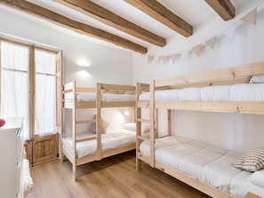 A bunk bed room with wooden beams, white walls, and a window with curtains. - Apartment 'Pèndol' with Balcony, Wi-Fi and Air Conditioning (Solsona)