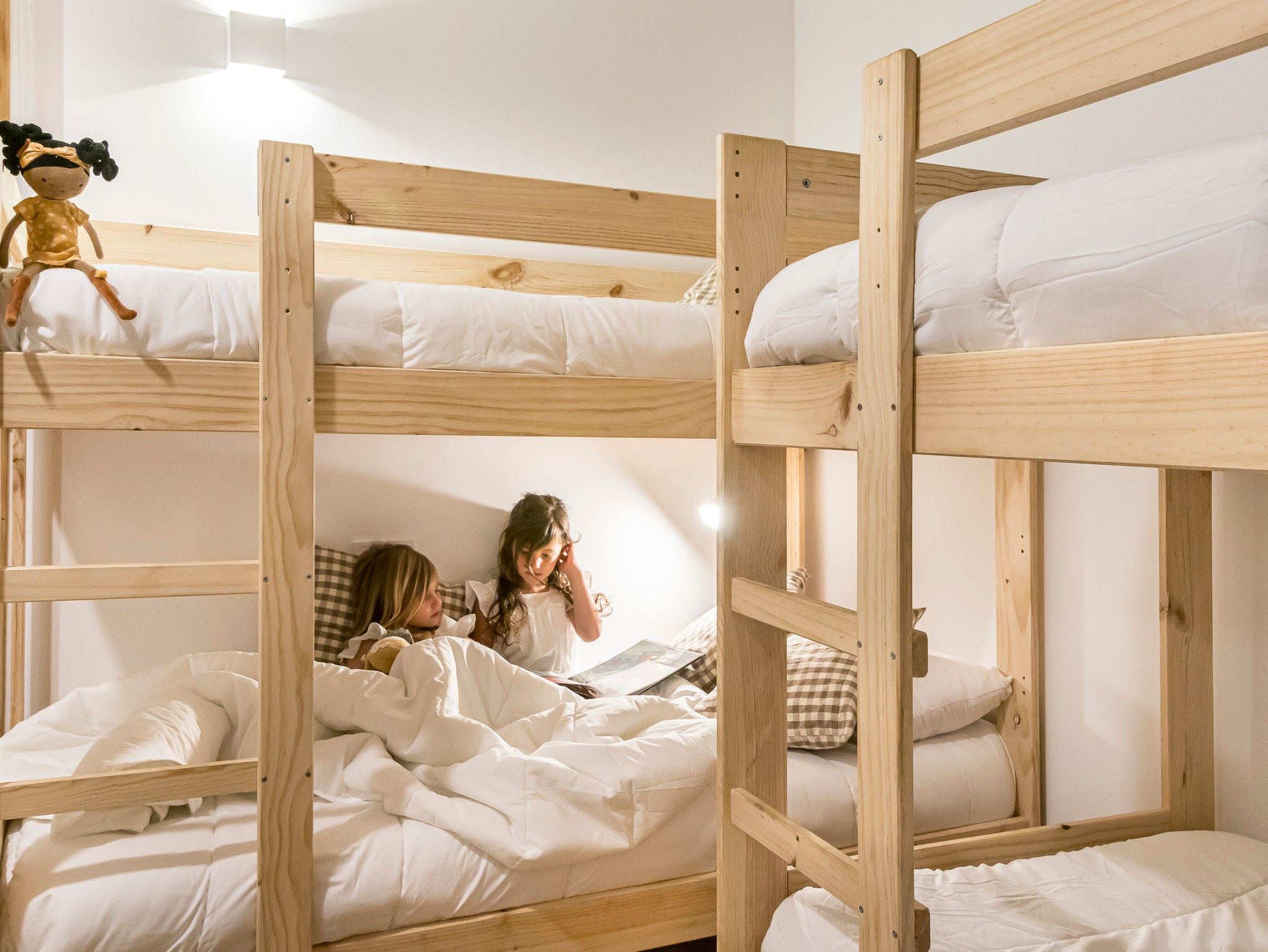 Tweepersoonsbed met witte lakens en een popje op het bovenste bed.