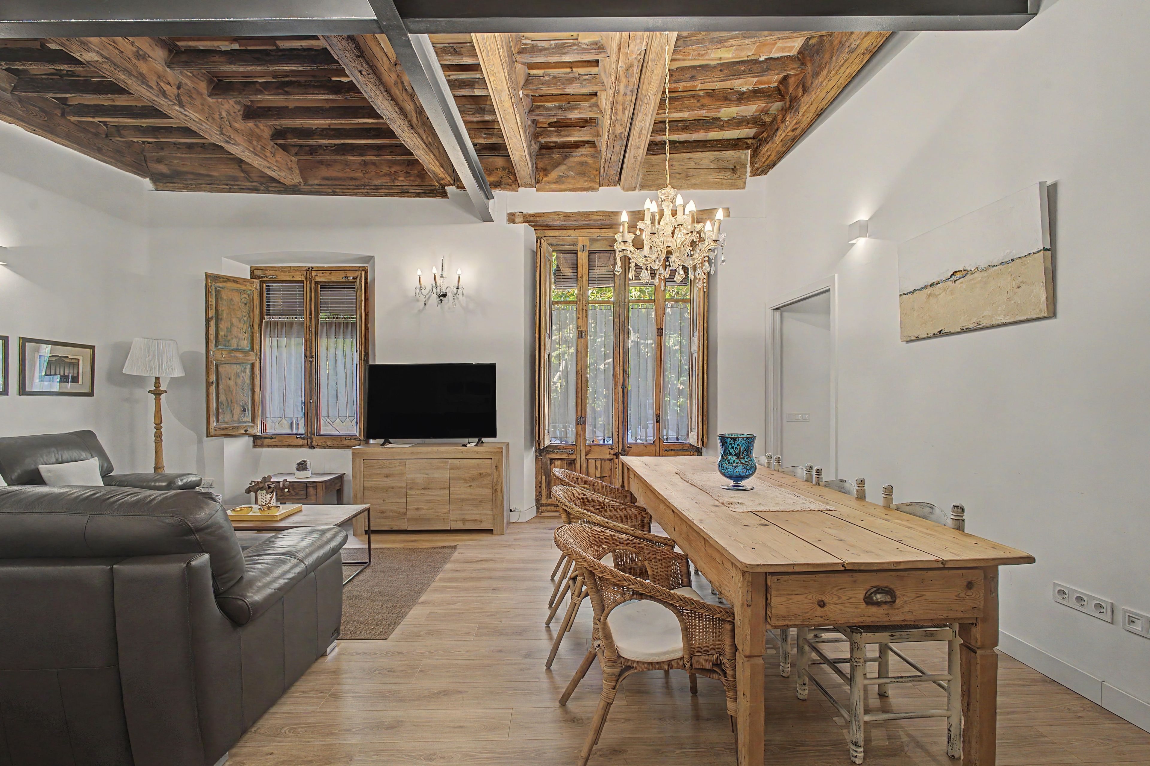 Un salon moderne avec un canapé, un téléviseur, une table à manger en bois et un lustre.