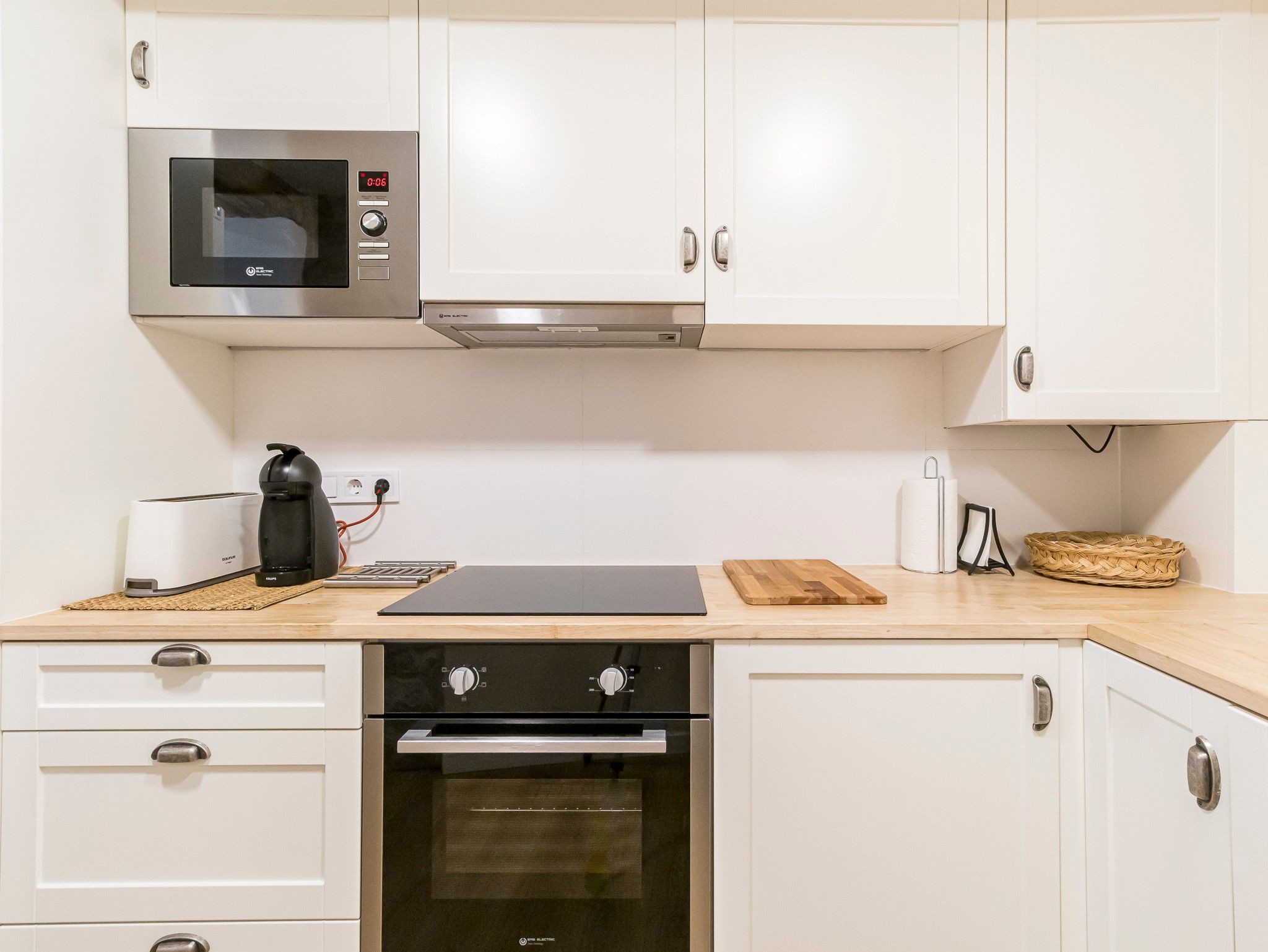 A modern kitchen with white cabinets, a built-in microwave, a coffee maker, and a toaster.
