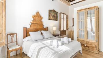 Un dormitorio con una cama de madera, una silla, una mesita de noche, una lámpara y un ventanal con cortinas.