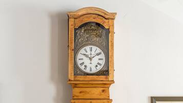 A tall grandfather clock with a wooden base and ornate carvings, mounted on a plain wall.