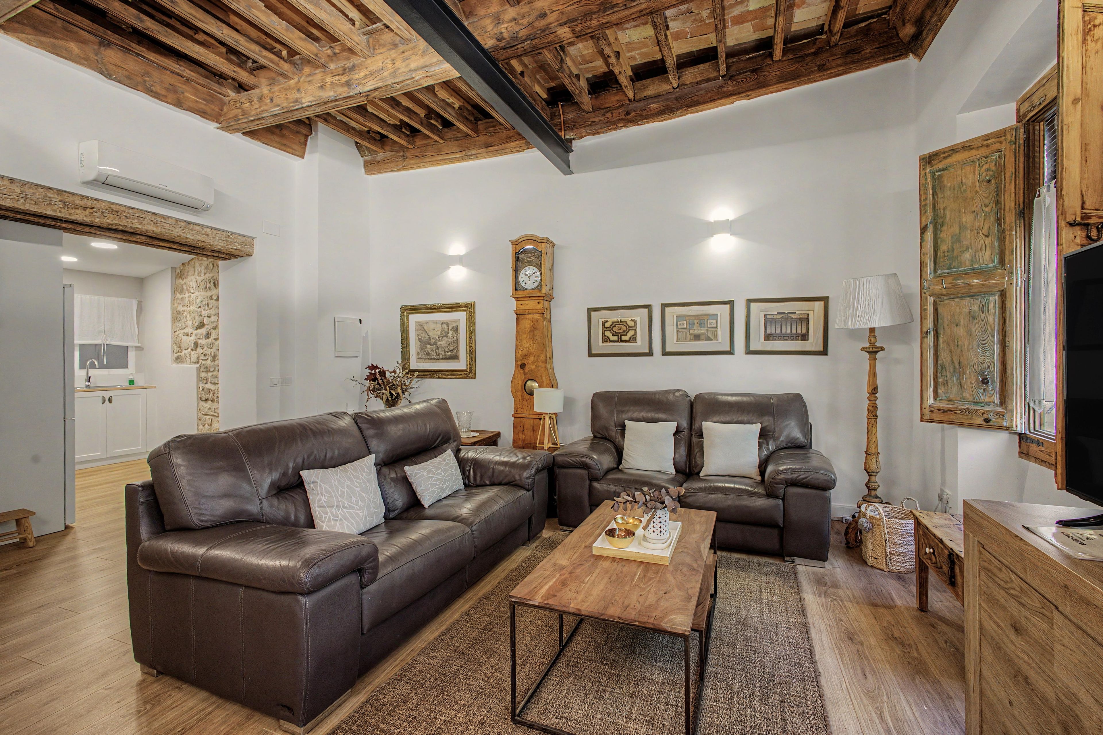 A living room with a brown leather sofa, a wooden coffee table, and a stone wall.