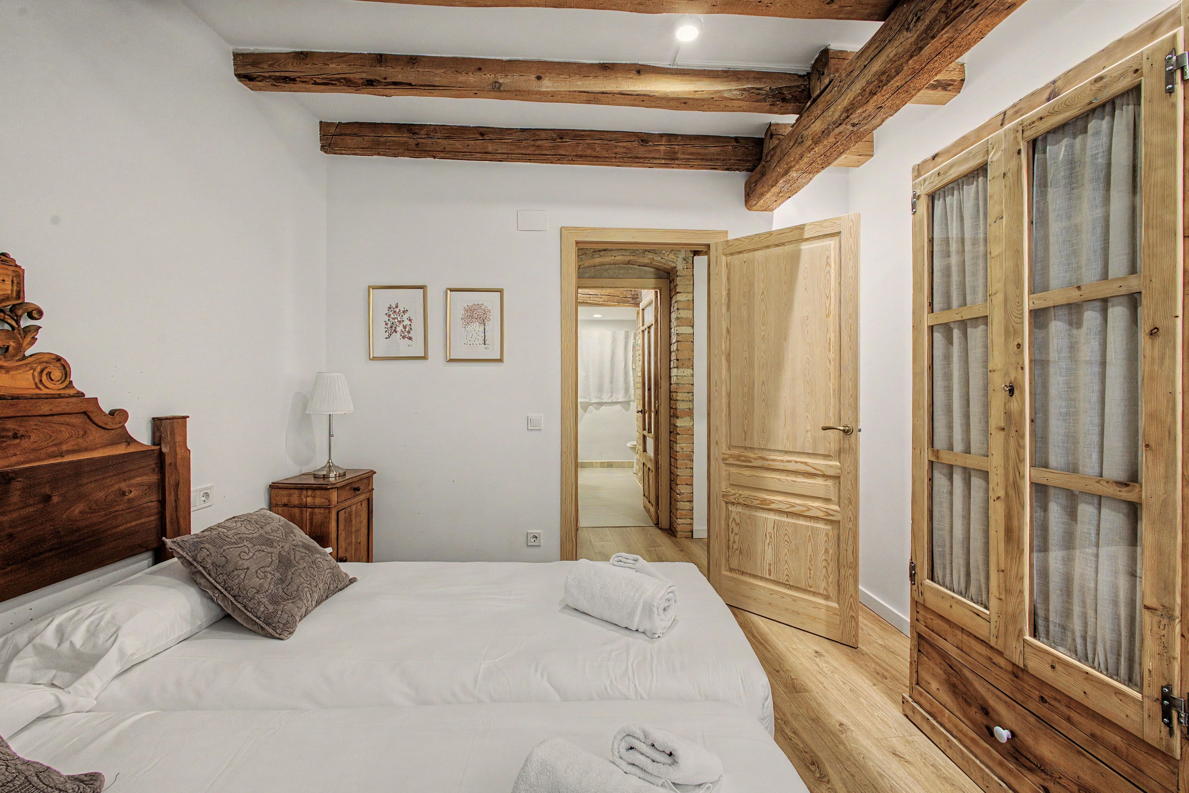 Un dormitorio con una cama grande, cabecera de madera, una mesita de noche, una lámpara y dos cuadros en la pared.