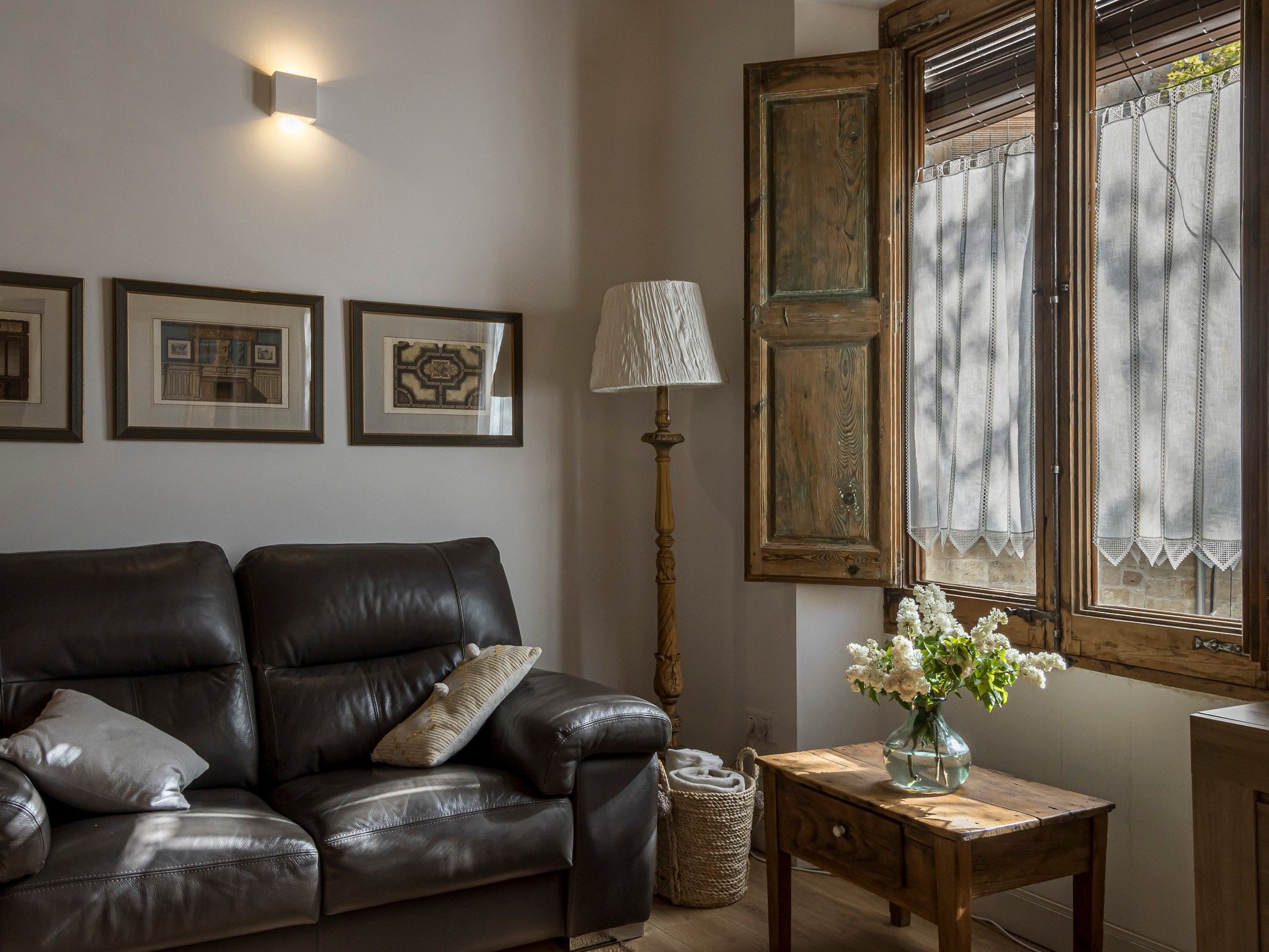 A living room with a leather sofa, a lamp, a vase with flowers, and framed pictures on the wall.