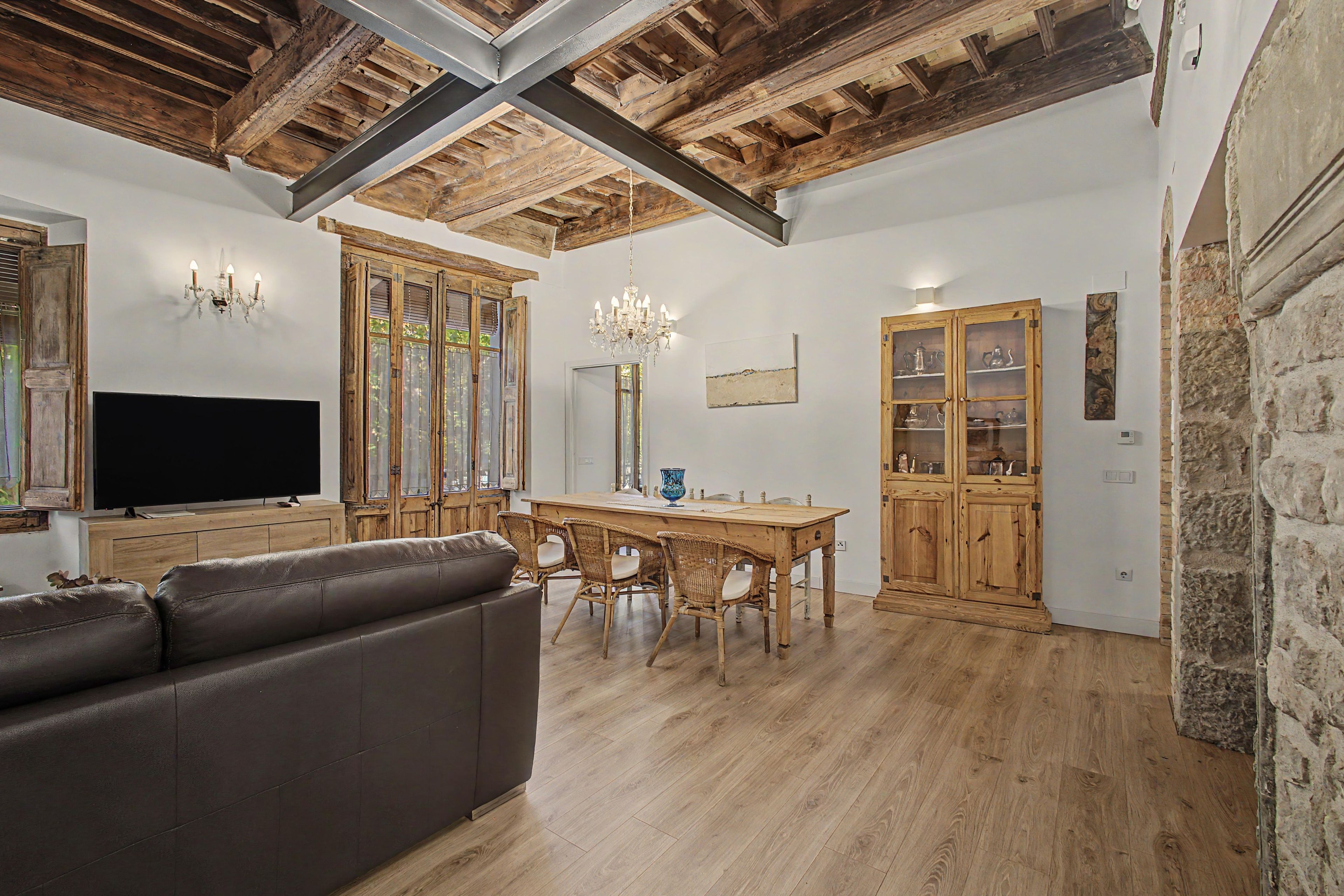 A living room with a flat-screen TV, a leather sofa, wooden dining table, and chairs.