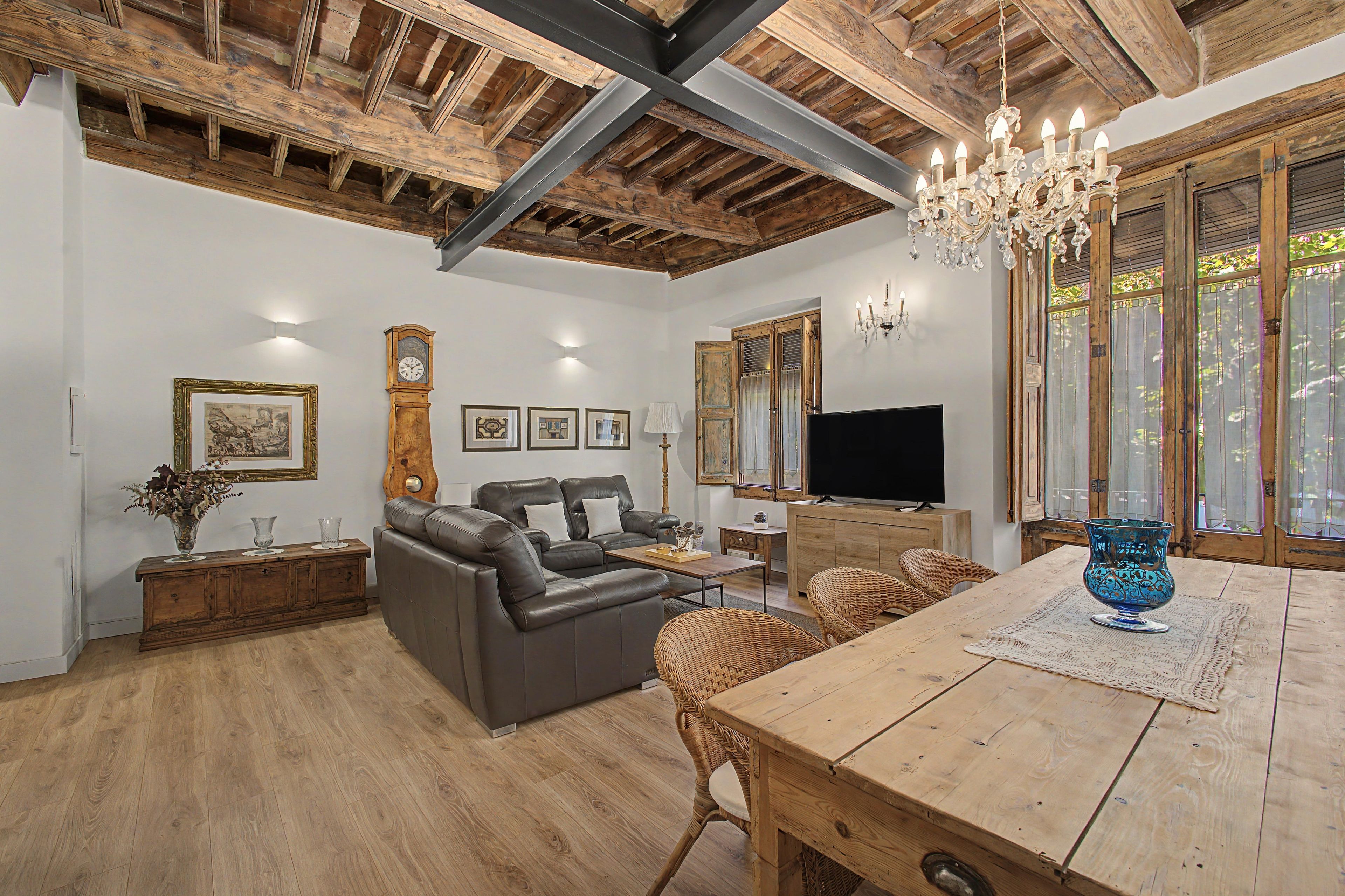 Een ruime woonkamer met een houten plafond, een kroonluchter, een bank, een eettafel en een televisie.