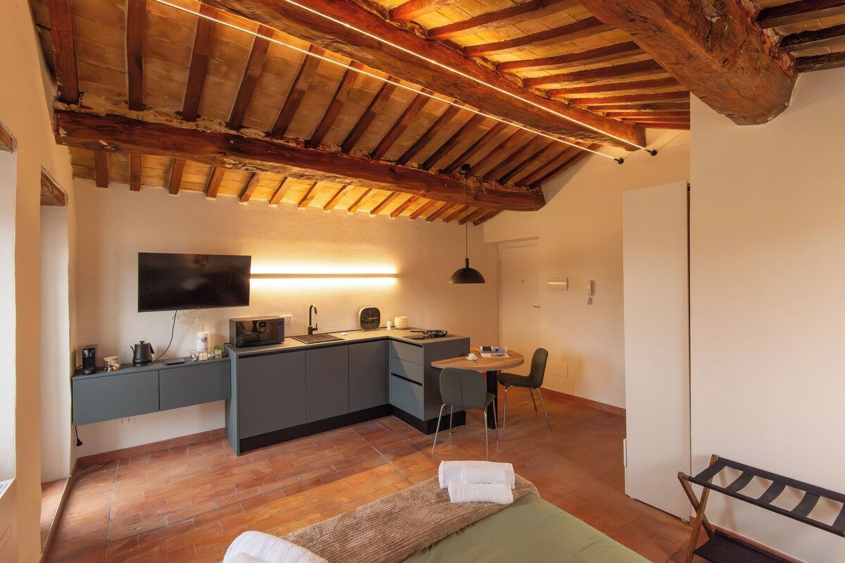 A compact kitchen with a flat-screen TV, a dining area with a table and chairs, and a bed with a bench.