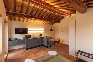 Een compacte keuken met een flatscreen televisie, een zithoek met een tafel en stoelen, en een bed met een bankje.