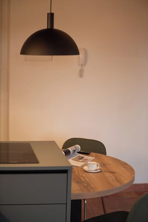 A dining area with a round wooden table, a chair, a telephone, and a black pendant light. - Chic Design Condo with Fast WiFi Near Assisi (Rivotorto)