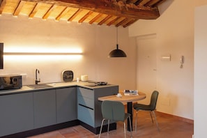 Een kleine keuken met een inbouwmagnetron, een spoelbak en een eethoek met een tafel en stoelen.