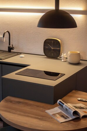 A modern kitchen with a built-in sink, a black clock, a white mug, and a wooden table with a magazine. - Chic Design Condo with Fast WiFi Near Assisi (Rivotorto)