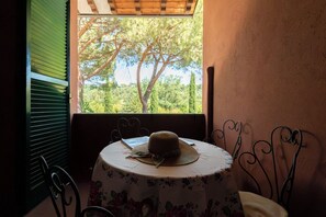 Une table recouverte d’une nappe à motifs floraux, sur laquelle est posé un chapeau, placée près d’une fenêtre donnant sur des arbres.