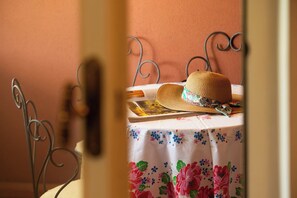 A room with a metal bed frame, a table with a floral tablecloth, and a straw hat on the table. - Garden Retreat Apt w/ Parking, Near Perugia Center (Perugia)