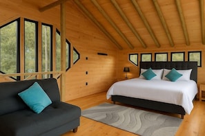 Ein Schlafzimmer einer Holzhütte mit einem Bett, einer Couch und großen Fenstern.