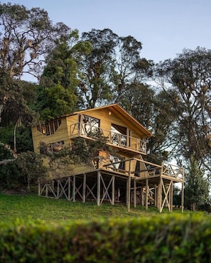 A two-story wooden house with a balcony, surrounded by trees. - Neusa Hills Glamping (Tausa)