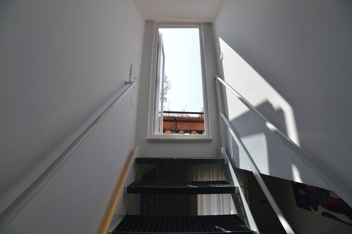 A narrow stairway with a window at the top, leading to a landing.
