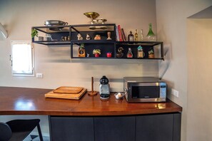 A kitchen with a wooden countertop, a coffee maker, a microwave, and shelves with various kitchen items.