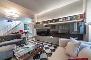A modern living room with a checkered floor, a sofa, a coffee table, and a flat-screen TV mounted on the wall. - Deseos Panoramic Terrace Condo w/View of Torre degli (Perugia)