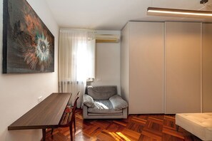 A room with a wooden floor, a grey sofa, a dining table with chairs, a painting on the wall, and an air conditioning unit. - Deseos Panoramic Terrace Condo w/View of Torre degli (Perugia)
