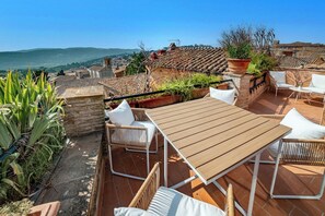 A rooftop terrace with a wooden table and wicker chairs, overlooking a cityscape with terracotta roofs. - Deseos Panoramic Terrace Condo w/View of Torre degli (Perugia)