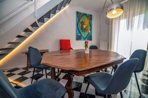 A dining area with a round wooden table, blue chairs, a red cushion, and a large abstract painting on the wall. - Deseos Panoramic Terrace Condo w/View of Torre degli (Perugia)