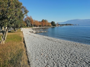 A pebbled beach with a clear view of the water and distant mountains. - Sunflower Apartment (San Felice del Benaco)