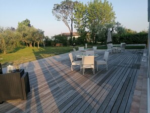 A wooden deck with outdoor furniture, including a table and chairs, surrounded by greenery and trees. - Sunflower Apartment (San Felice del Benaco)