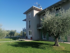 A two-story building with a balcony, a small garden, and a tree. - Sunflower Apartment (San Felice del Benaco)