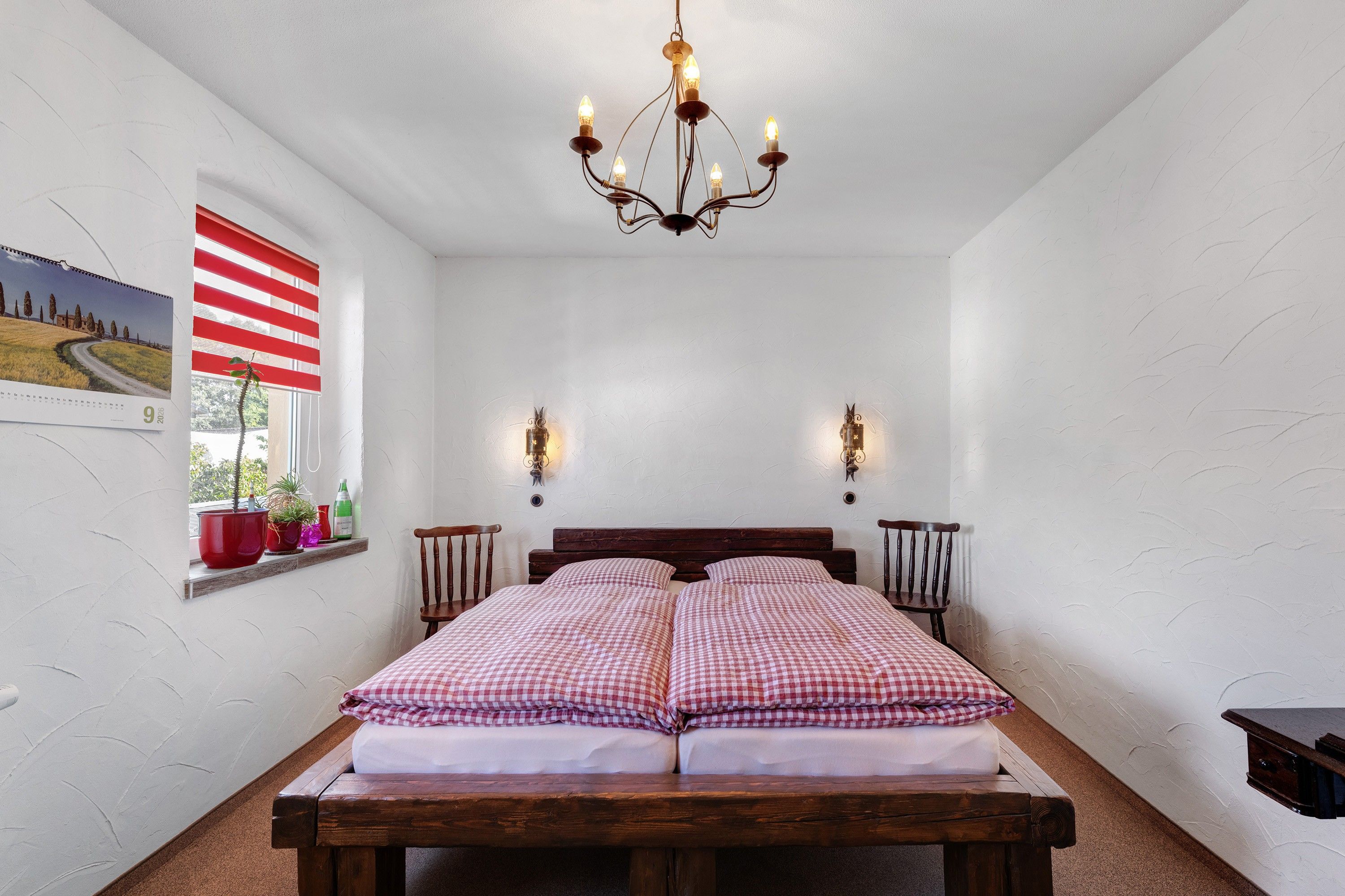 Ein Schlafzimmer mit einem hölzernen Bett, einer Kristallleuchter, einem Fenster mit Jalousien und Wandleuchten.