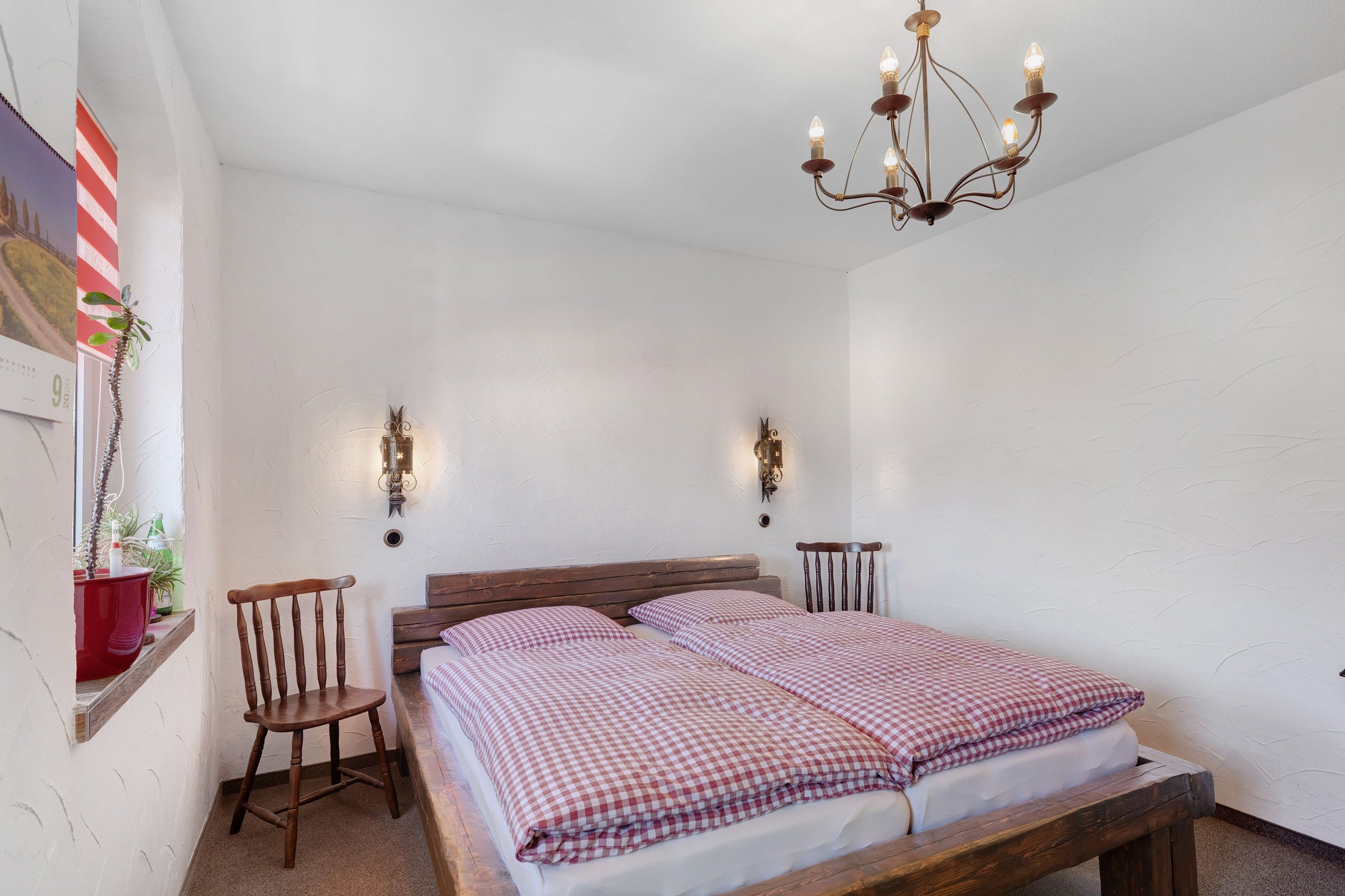 A bedroom with a wooden bed, two wall-mounted lamps, and a chandelier.