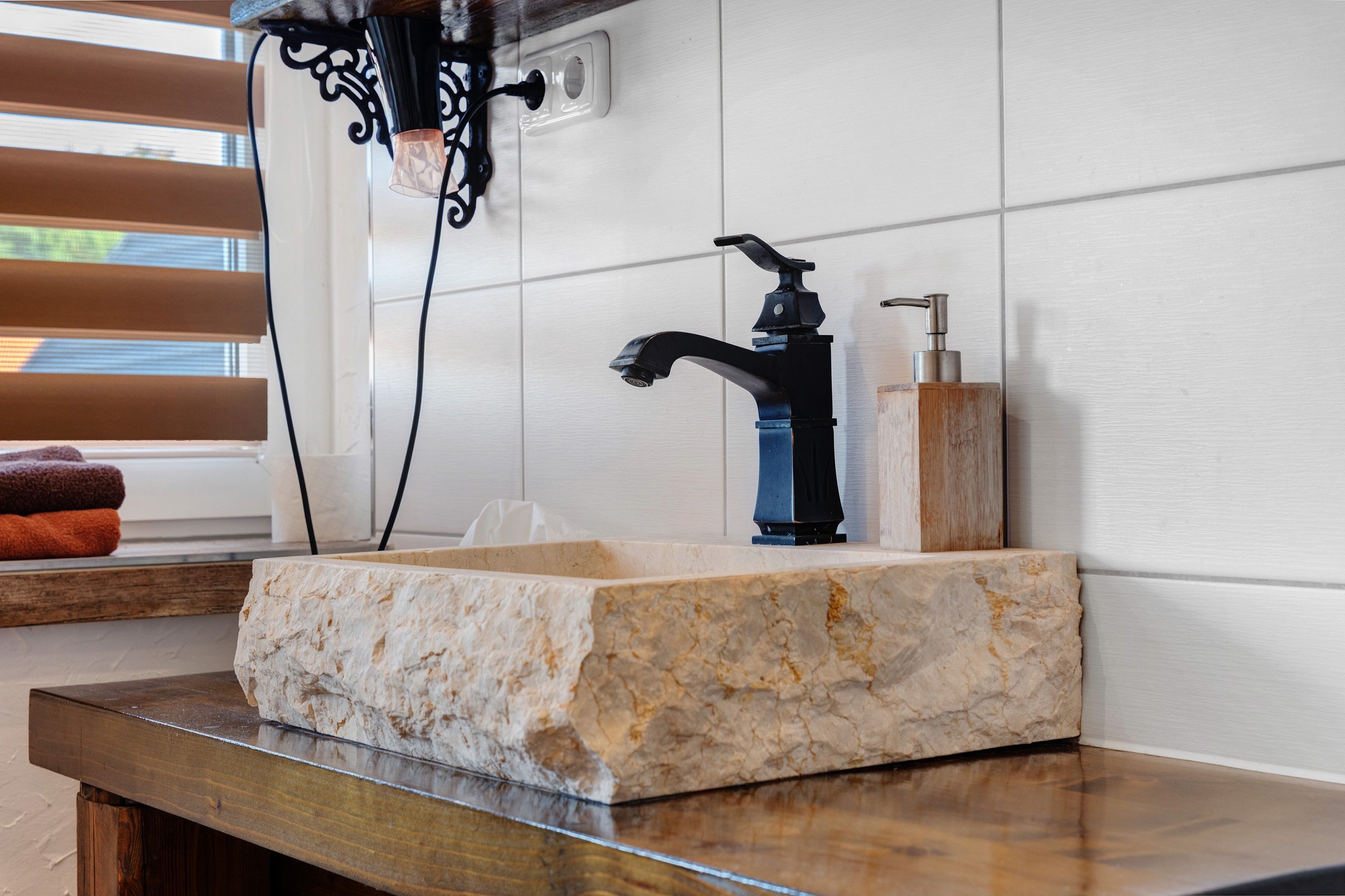 A bathroom with a marble sink, black faucet, and a wooden soap dispenser.