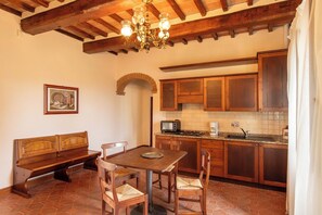 A cozy kitchen with wooden cabinets, a dining table with chairs, a bench, and a chandelier. - Villa Missiano Unità Orione con Piscina (Panicale)