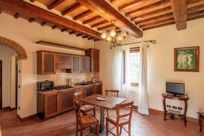 Une cuisine avec des meubles en bois, une table à manger avec des chaises, un lustre et un téléviseur posé sur un meuble.
