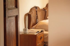 Une table de chevet en bois, avec une tasse et un livre ouvert, placée à côté d’un lit doté d’une tête de lit en osier.