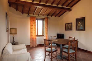 A dining area with a wooden table and chairs, a sofa, a lamp, and a window with curtains. - Villa Missiano Unità Pegaso con Piscina (Panicale)