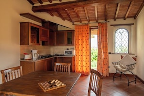 A kitchen with wooden cabinets, a dining table with chairs, a coffee maker, and a microwave. - Villa Missiano Unità Pegaso con Piscina (Panicale)