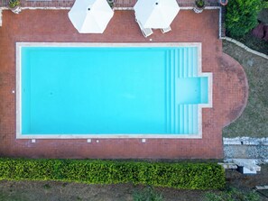 An aerial view of a rectangular swimming pool with a brick border, surrounded by a grassy area and a stone wall. - La Fenice Apartment: Pool, BBQ, Free Parking (Panicale)