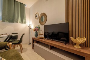 Een moderne woonkamer met een flatscreen televisie, een houten bankje, een rieten mand en een vaas met bloemen.