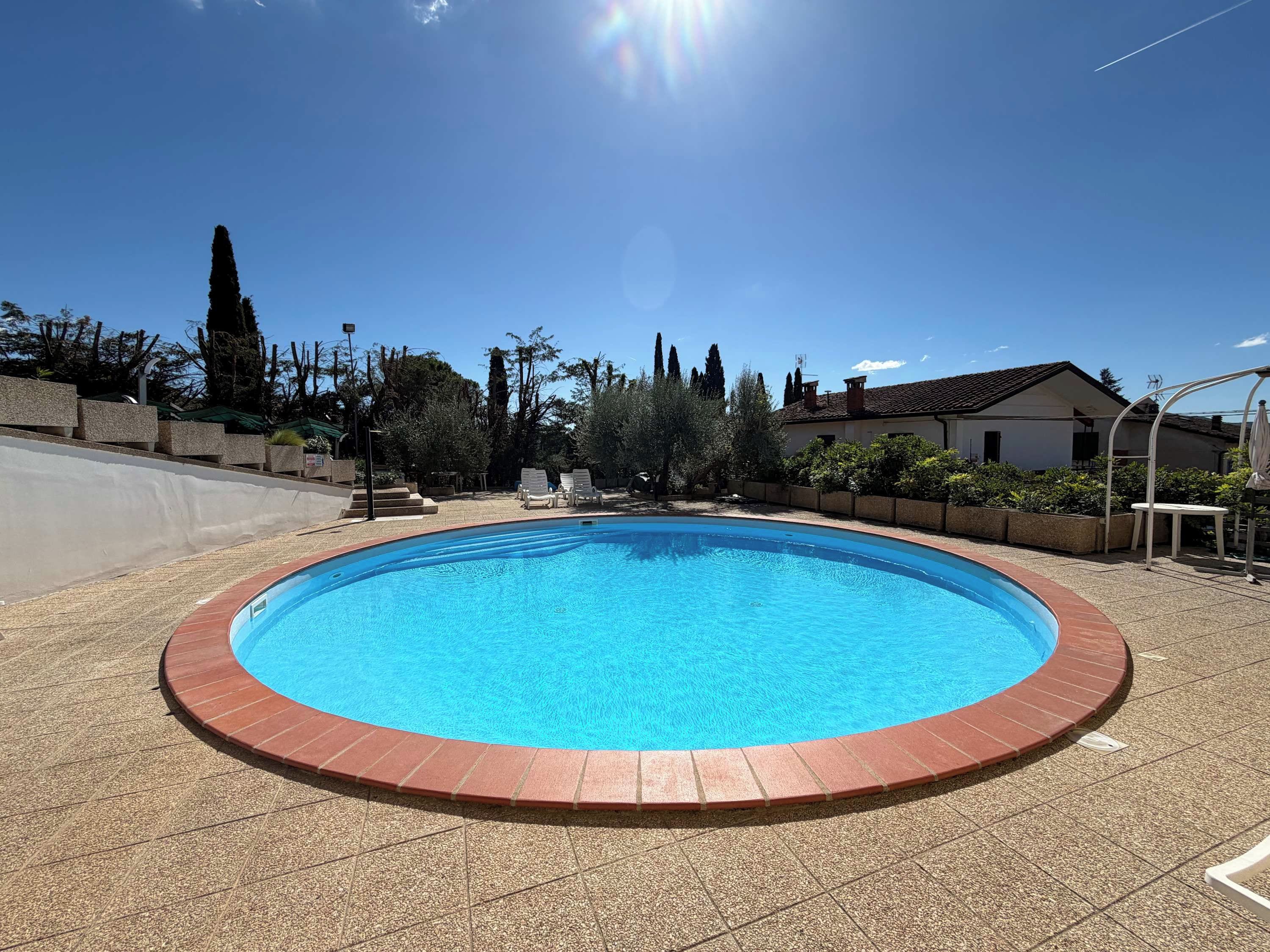 Una piscina circular con borde rojo, rodeada por un deck con mosaicos de piedrecitas.
