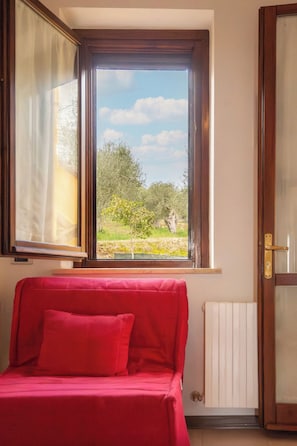 A room with a red sofa, a window with a view of greenery, and a radiator. - Lake View Apt. w/ Wi-Fi & Parking in San Feliciano (San Feliciano)