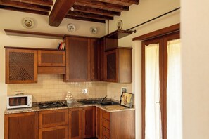 A kitchen with wooden cabinets, a microwave, a stove, and a sink. - Villa Missiano Unità Perseo con Piscina (Panicale)
