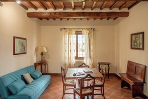 A dining area with a wooden table, chairs, a sofa, and a window with curtains. - Villa Missiano Unità Perseo con Piscina (Panicale)
