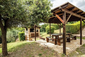 An outdoor patio with a stone table and benches, a wooden pergola, and a stone fireplace. - Villa Missiano Unità Perseo con Piscina (Panicale)